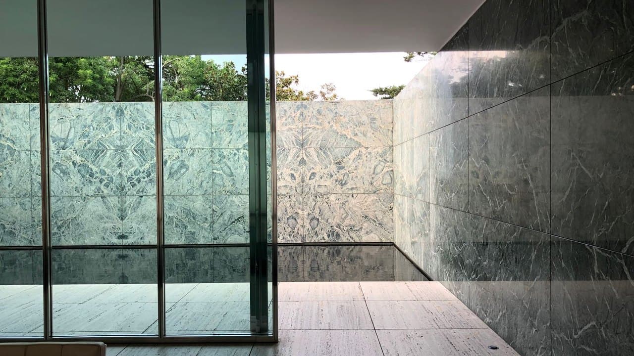 Interior of the Barcelona Pavilion by Mies van der Rohe, with glass walls, a stone wall and a reflecting pool beyond