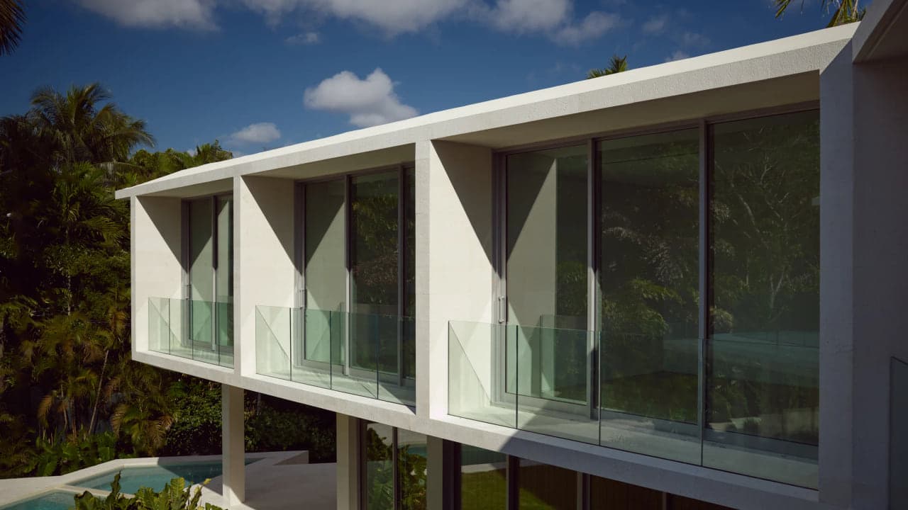 Cantilevered travertine and glass facade of a Coconut Grove residence over tree canopy and a pool deck, with no visible interior furnishings or people
