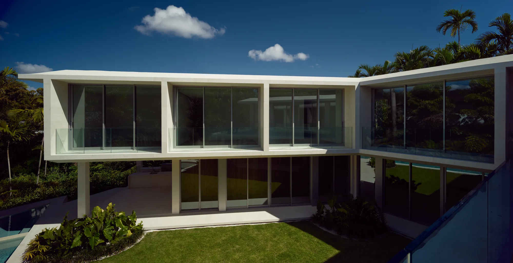 The finished Ingraham Residence in Coconut Grove, Miami: glass and stone facade, pool, and lawn, the same home shown in Luxom's empty lot to finished home timelapse