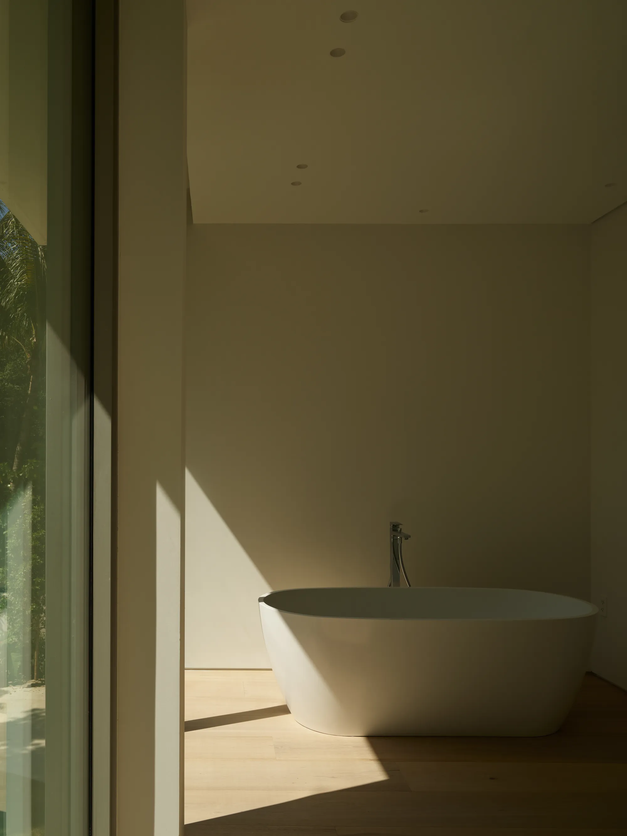 Freestanding tub set against a travertine wall in the primary bathroom of the Ingraham Residence by LUXOM, Miami