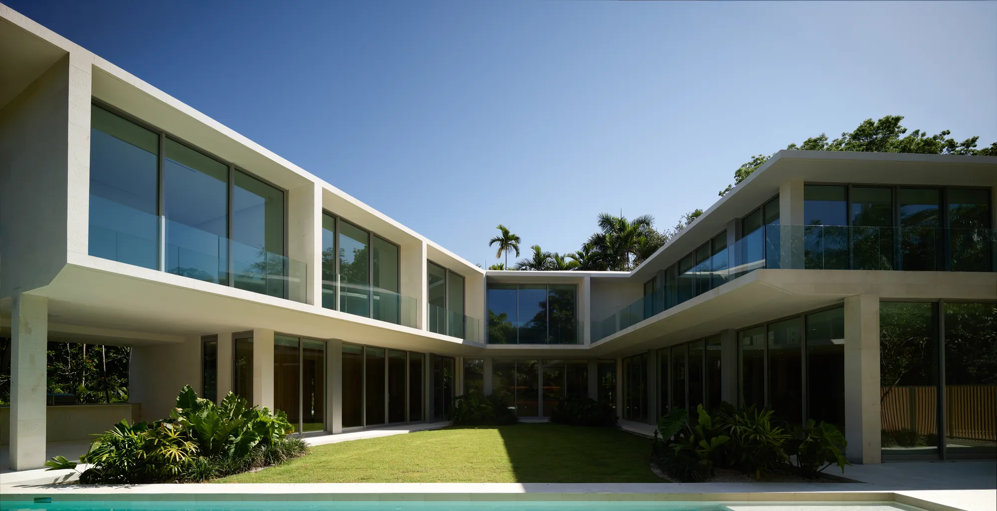 Ingraham Residence in Coconut Grove by LUXOM, two glass and stone wings wrapping a center lawn and pool around an open courtyard