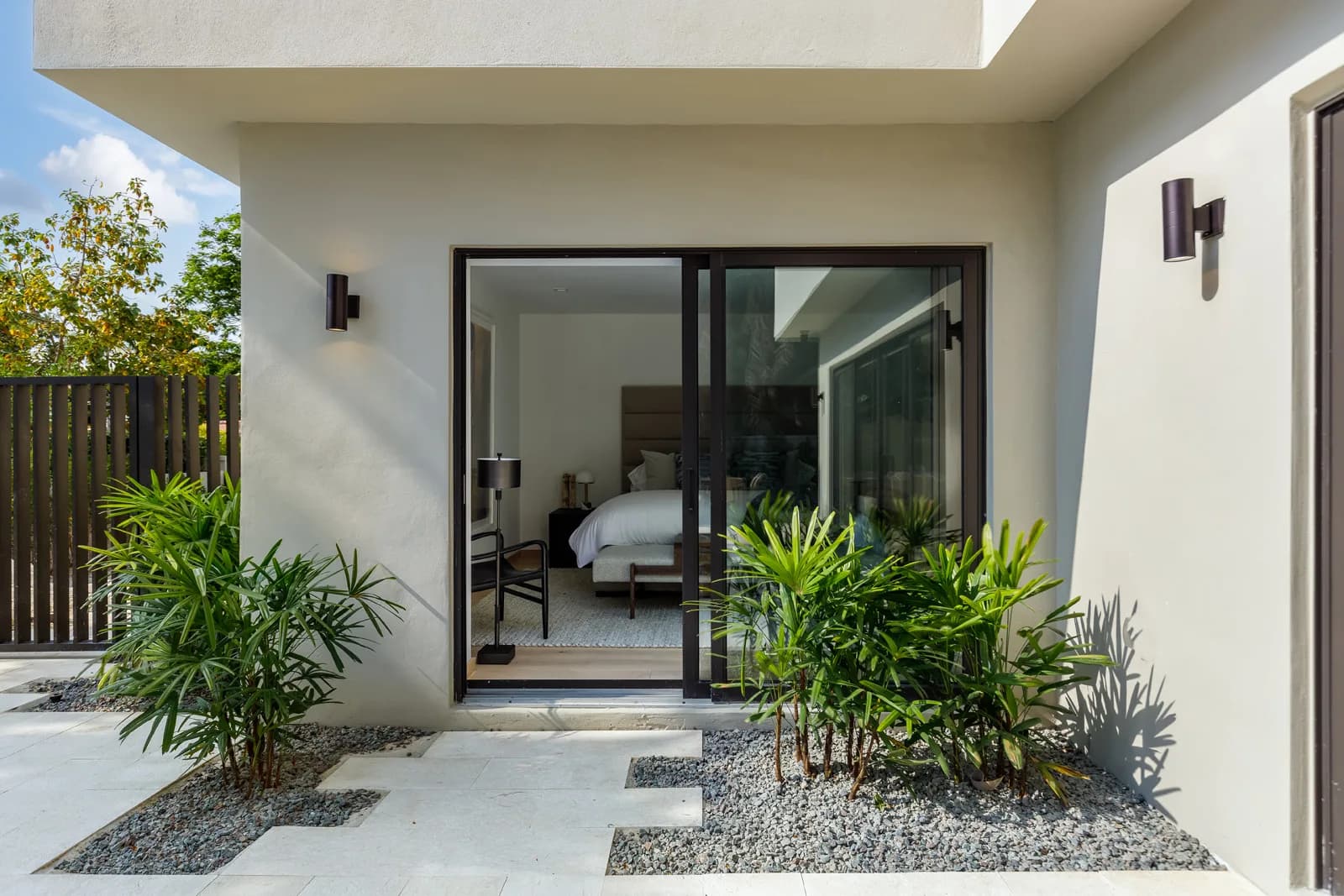 The primary bedroom at the Samana Residence in Coconut Grove seen through its glass sliding doors, the finished room behind Luxom's block, conduit, plaster and paint fit-out sequence