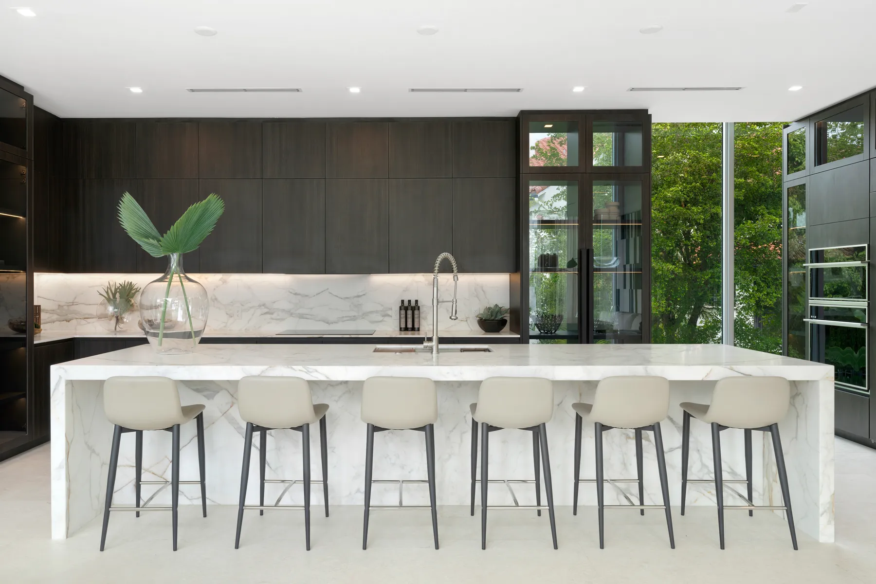 The finished kitchen at Luxom's Crystal Residence in Coconut Grove, with one continuous run of book matched stone across the island, the perimeter counter and the backsplash against dark wood cabinetry