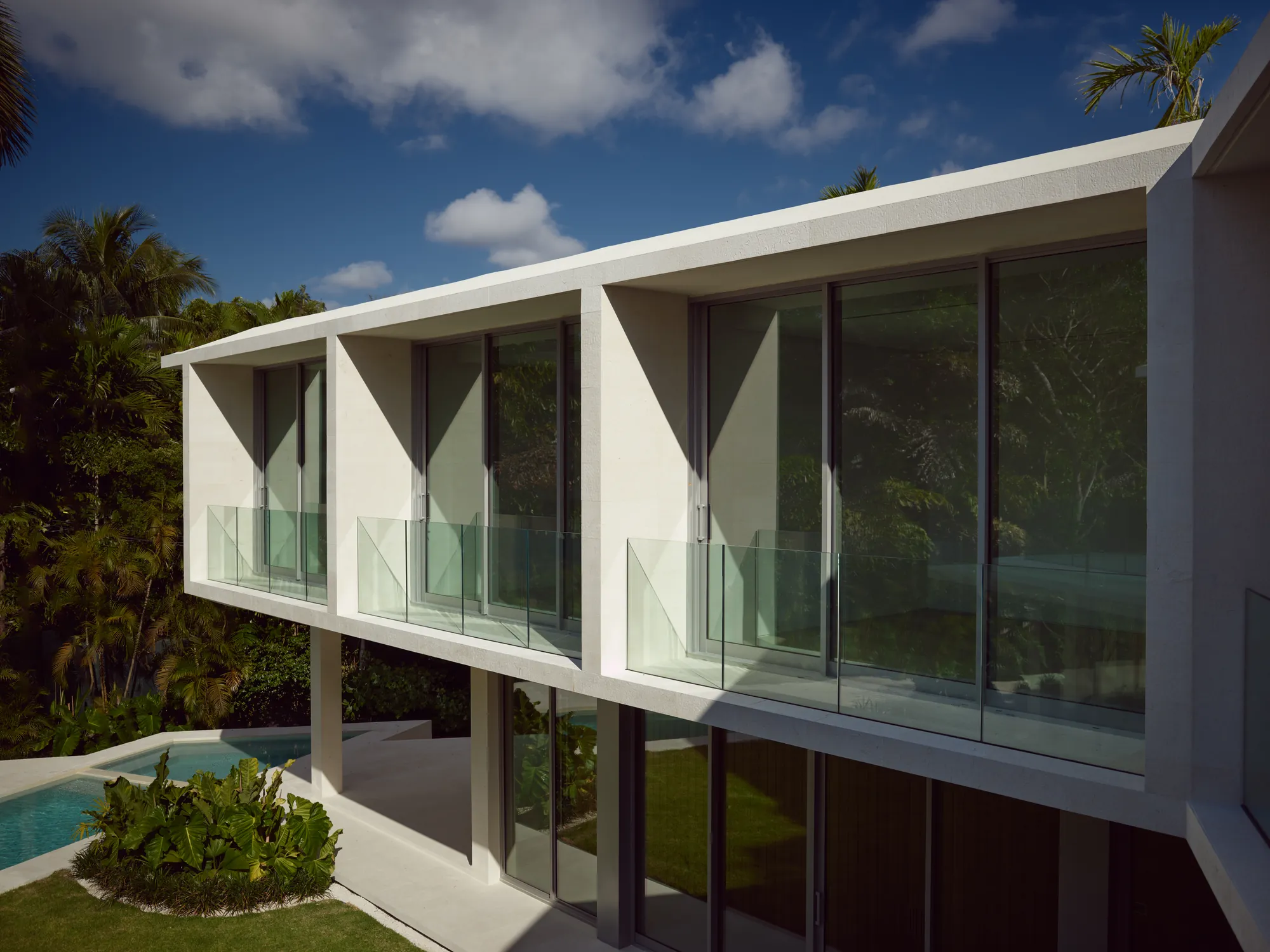 Cantilevered white stucco upper floor of the Ingraham Residence in Coconut Grove, with glass balconies over a pool and palm trees