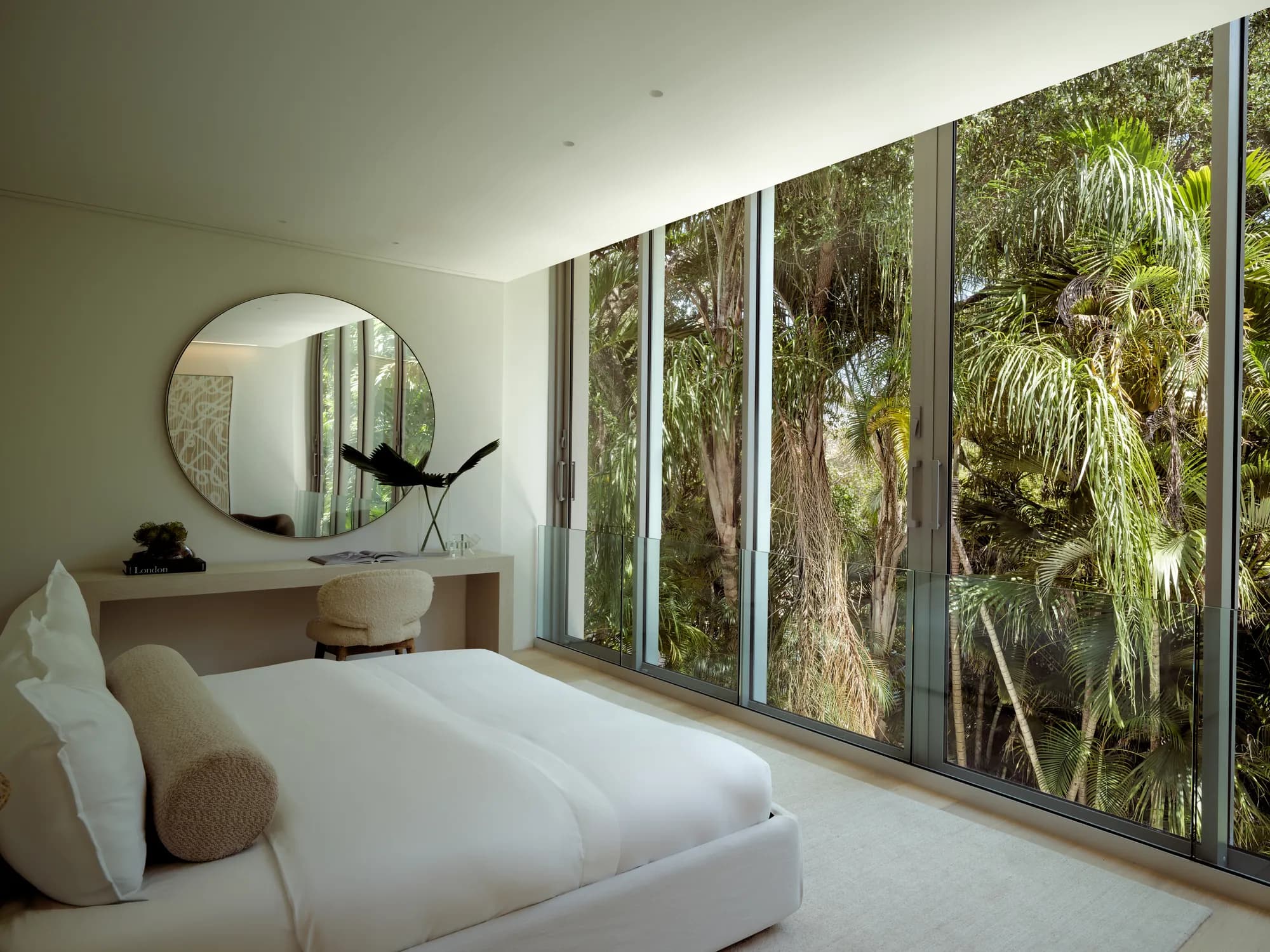 Primary bedroom at the Onaway Residence in Coconut Grove with floor to ceiling glass running the length of the room, palm canopy and morning light filling the space