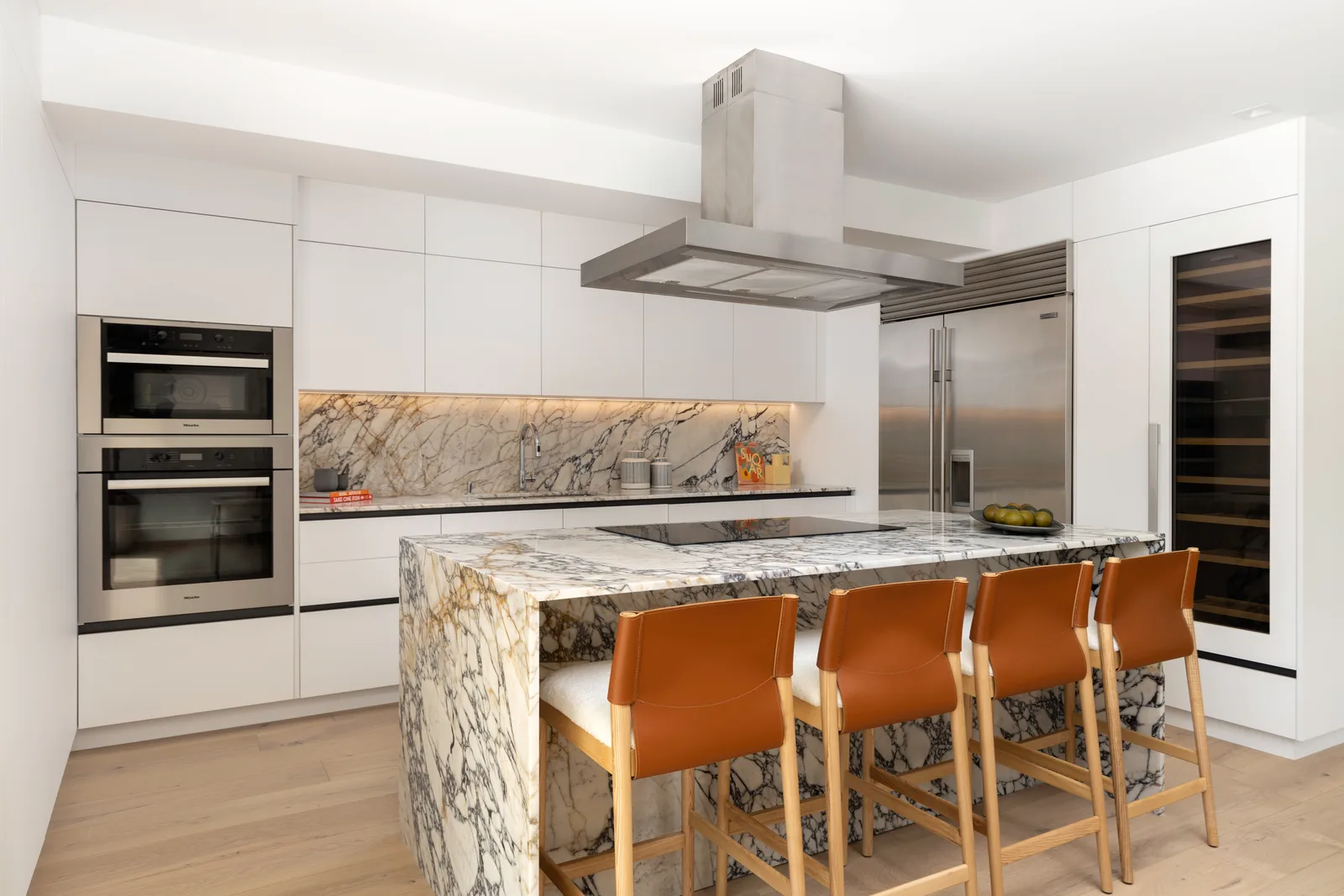 Calacatta gold marble waterfall island in the Samana Residence kitchen in Coconut Grove, Miami, with leather counter stools and a matching marble backsplash