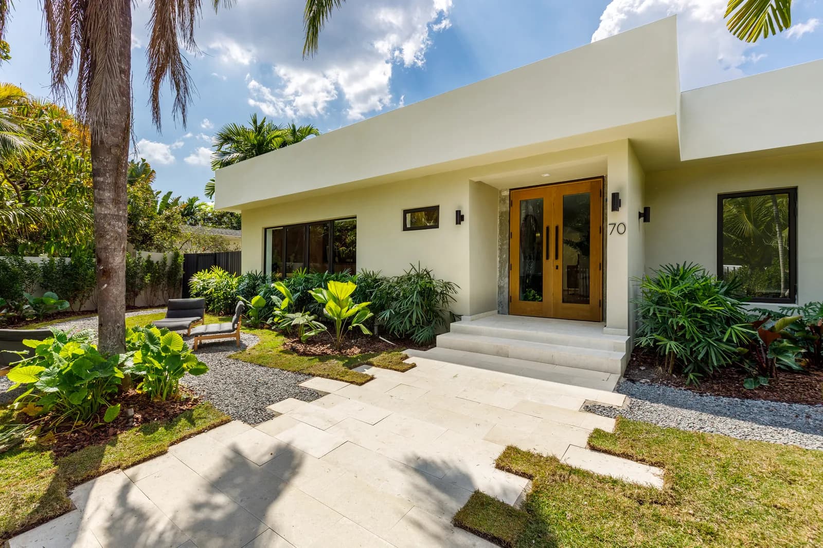 Modern white stucco entry to the Samana Residence in Coconut Grove, framed by tropical landscaping and a wood front door